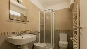 Un baño con lavamanos, bidé, inodoro y ducha con mampara de vidrio.