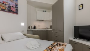Habitación de hotel con cama, televisión, zona de cocina y un cuadro en la pared.
