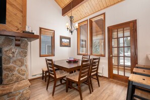 A dining area with a stone fireplace, wooden table, and chairs. There are windows with wooden frames and a chandelier. - 3BR Cozy Townhome | Walk to Town | Office, Patio (Winter Park)
