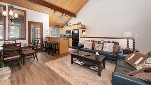 A spacious living room with a wooden ceiling, a sofa, a coffee table, and a dining area with chairs and a table. - 3BR Cozy Townhome | Walk to Town | Office, Patio (Winter Park)
