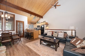 A spacious living room with a wooden ceiling, a sofa, a coffee table, and a dining area with chairs and a table. - 3BR Cozy Townhome | Walk to Town | Office, Patio (Winter Park)