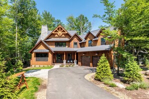 A large, multi-story wooden house with a stone chimney, a driveway, and a well-maintained garden with trees and shrubs. - Pemi Riverfront | Direct River and Swimming Access (Lincoln)