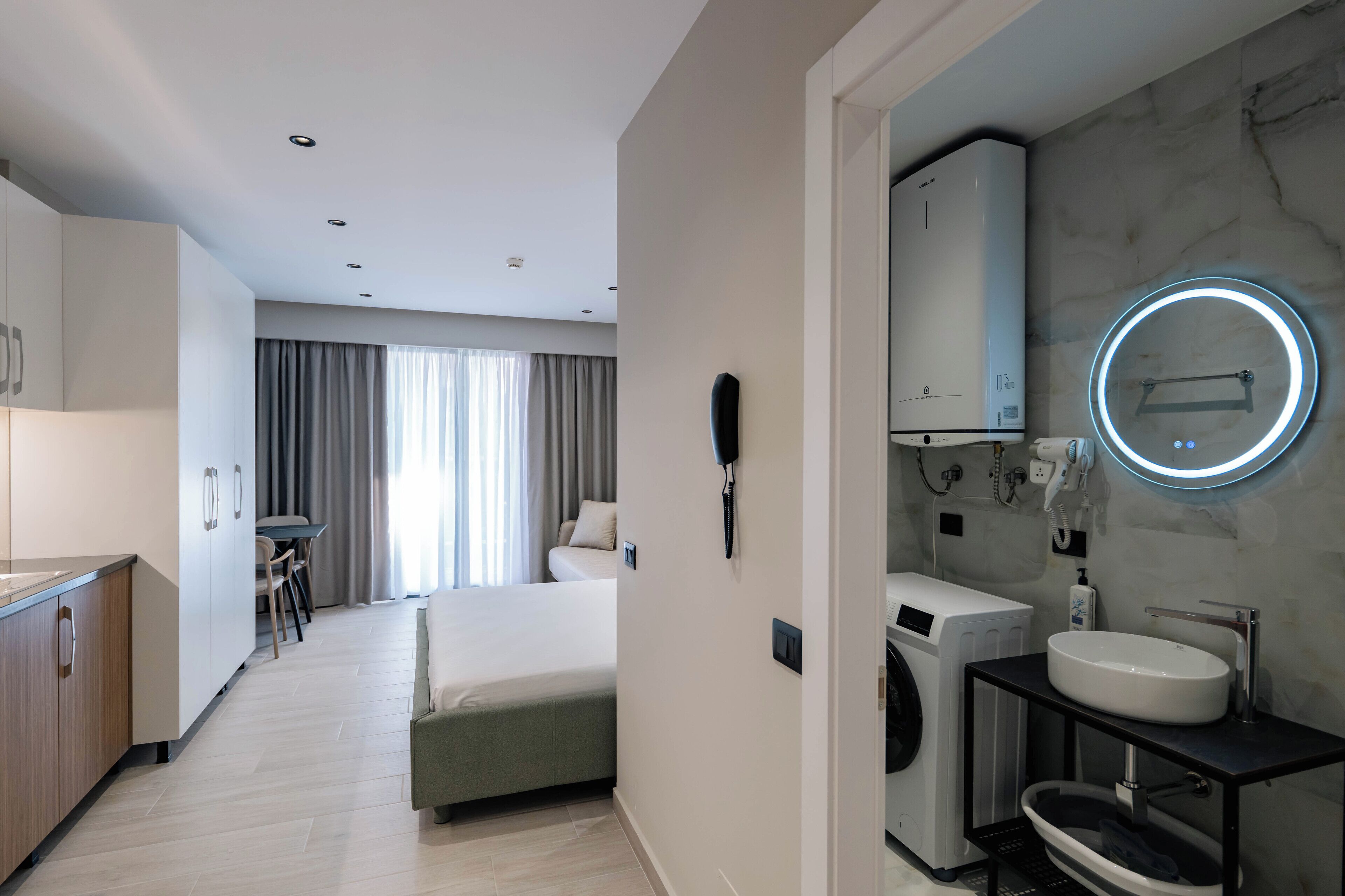 Una habitación de hotel moderna con una cama, un escritorio, una lavadora y un baño con lavamanos y espejo.
