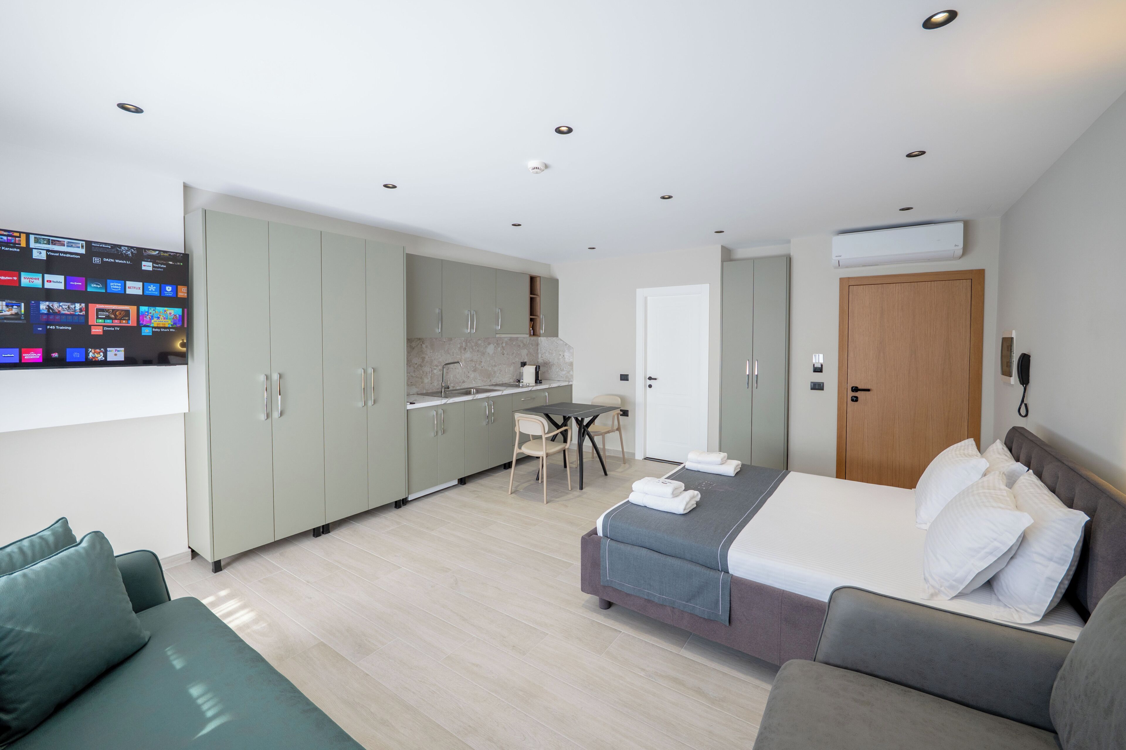 Ein modernes Hotelzimmer mit einem Bett, einer Couch, einem Esstisch und einer Küchenzeile.