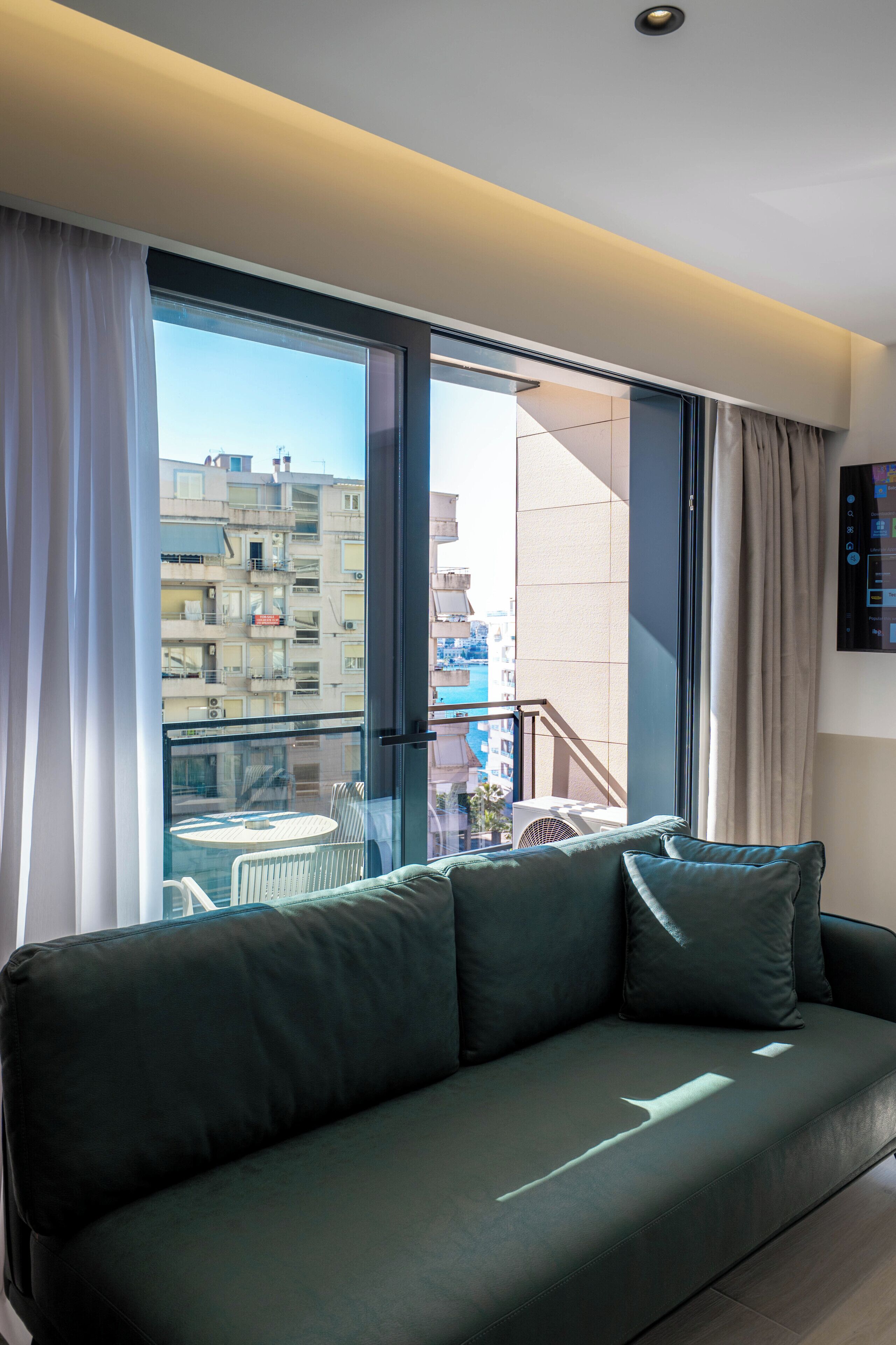 Una sala de estar moderna con un sofá verde, un ventanal de vidrio que da a un balcón y vistas de la ciudad.
