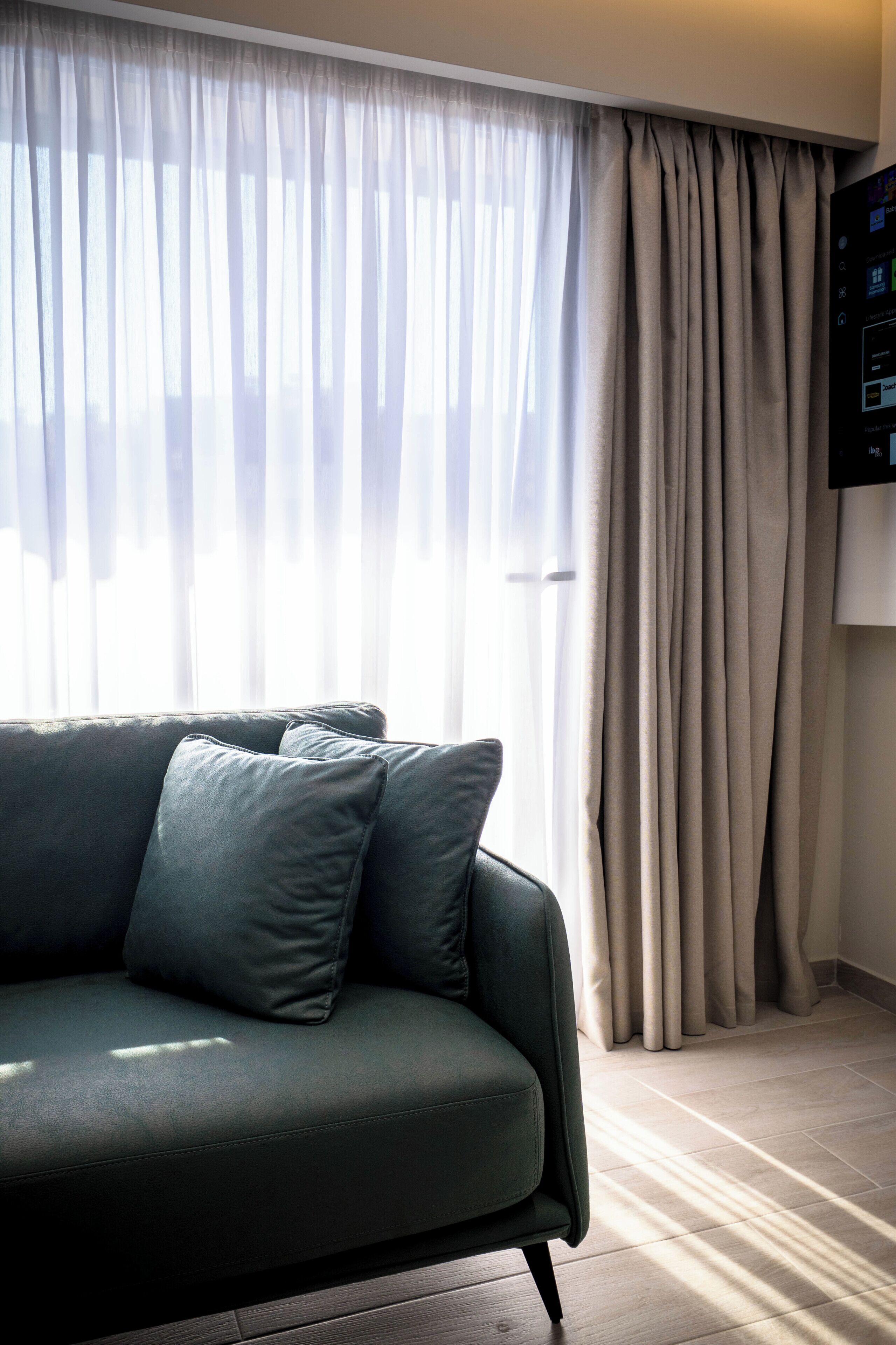 A living room with a sofa, a television on the wall, and a window with curtains.