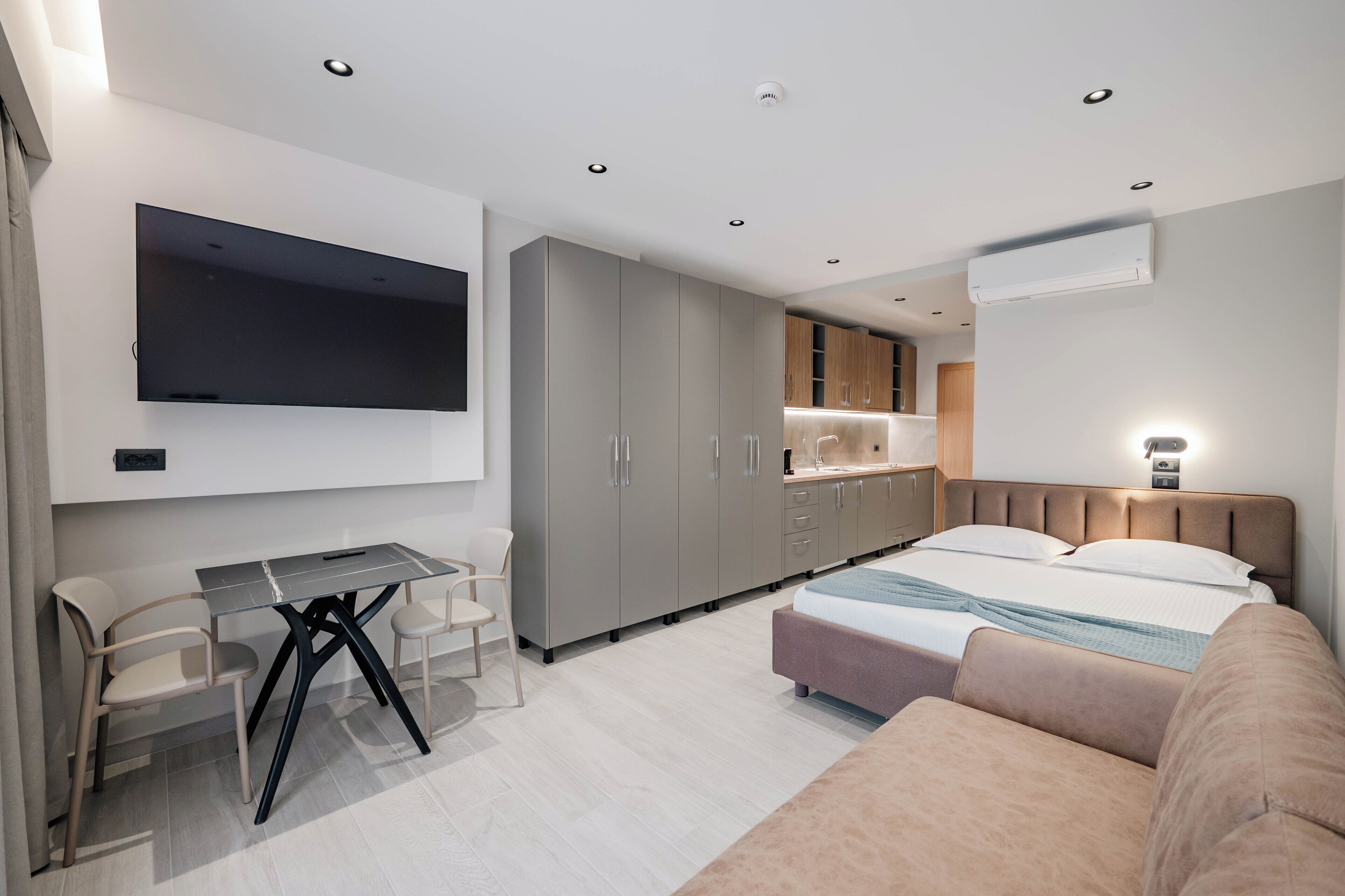 Quarto moderno com cama, mesa de cabeceira e TV fixada na parede.