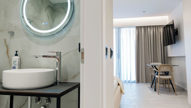 A modern bathroom with a large oval sink, a round mirror with LED lighting, and a marble wall. - Blas Residence (Sarande)