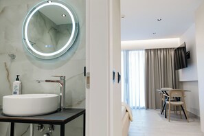 A modern bathroom with a large oval sink, a round mirror with LED lighting, and a marble wall. - Blas Residence (Sarande)
