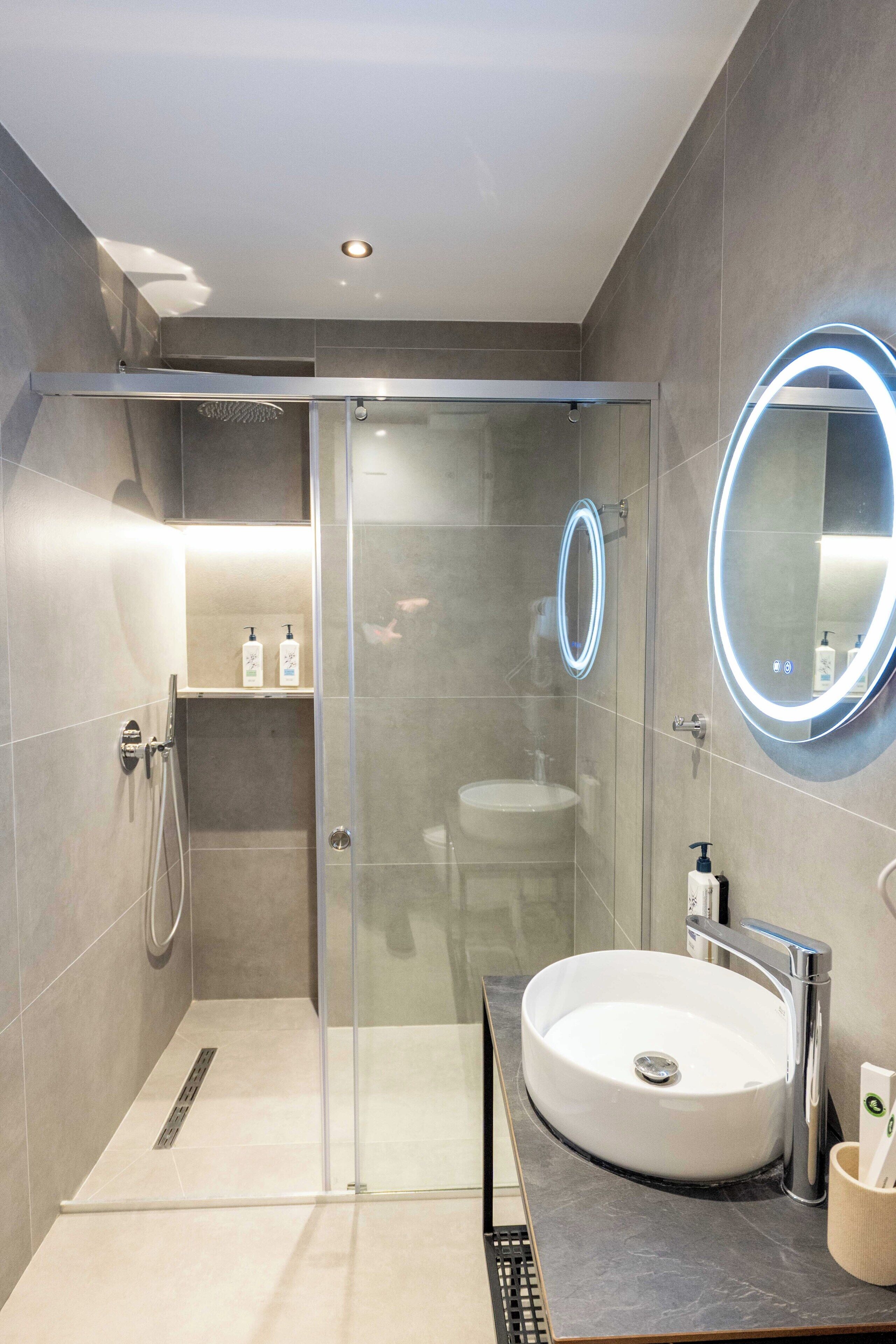 A modern bathroom with a glass-enclosed shower, a round mirror, and a white sink.