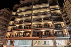 Een meerhoog hotel met balkons, een entrees op de begane grond en verlichte ramen.