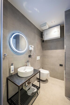 Un baño moderno con un espejo redondo, un lavamanos, un inodoro y un aire acondicionado de pared.