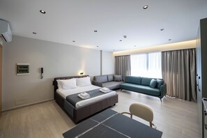 Una habitación de hotel moderna con una cama grande, un sofá, una mesa de comedor y vistas al exterior.