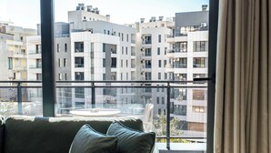 A modern living room with a large window, a green sofa, and a view of a cityscape. - Blas Residence (Sarande)