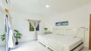 Een slaapkamer met een groot bed, een raam met gordijnen, een nachtkastje met een lamp en een potplant.