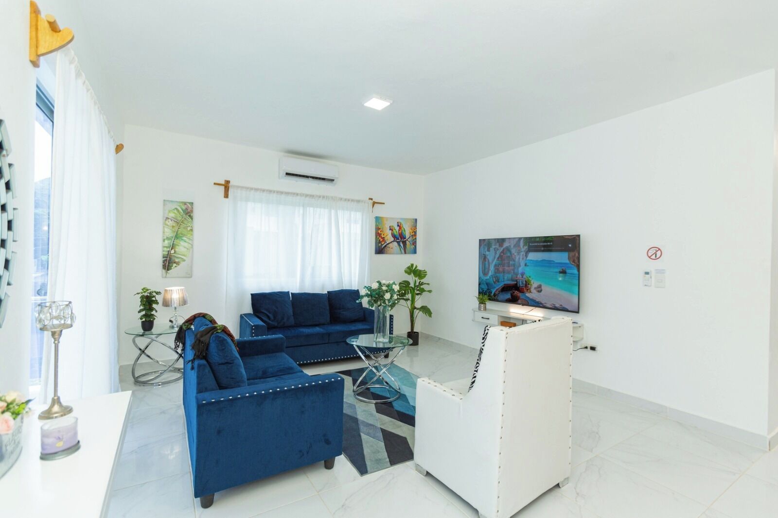 A modern living room with a blue sofa set, a glass coffee table, and a flat-screen TV.