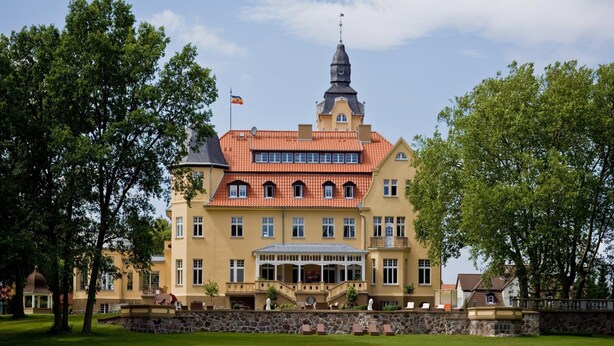 A large, two-story building with a prominent tower and a flag. - Reihenhaus Reiterchalet in Wendorf (Kuhlen-Wendorf)