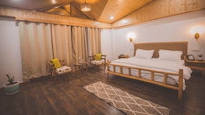 A bedroom with a wooden ceiling, a large bed, two bedside tables, a nightstand, a chair, a small table, and a potted plant. - NinYanWays Boutique Stay (Manali)