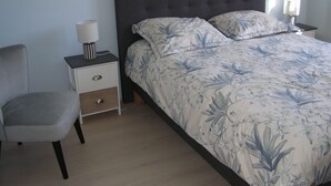 A bedroom with a bed, a chair, a nightstand, and a lamp.