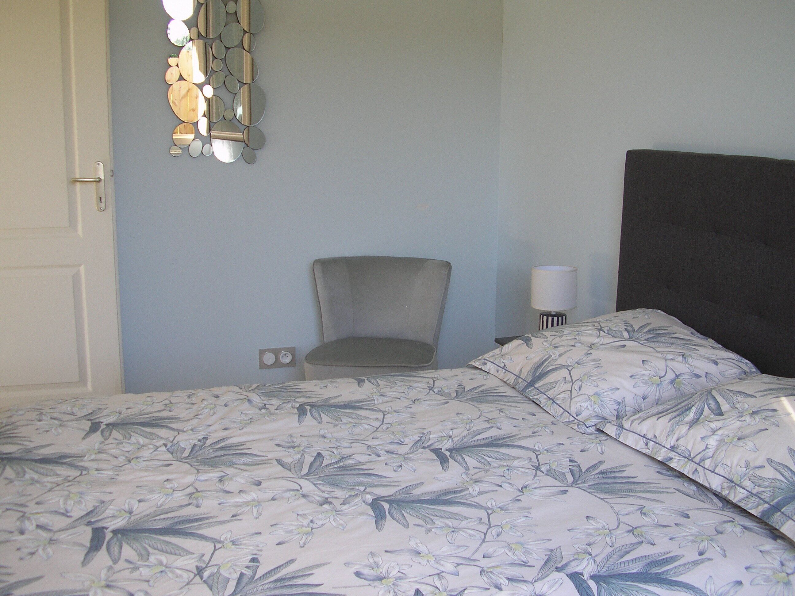A bedroom with a bed, a chair, a wall-mounted light fixture, and a power outlet.