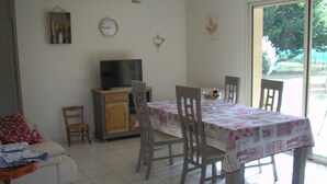 A dining area with a table set for four, a television on a cabinet, and a sofa with a floral pillow.