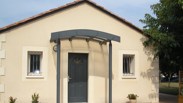 A building with a dark door, two windows with bars, and a small porch with a curved roof.