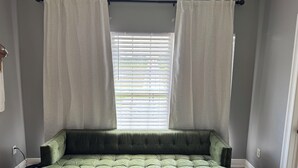 A room with a green sofa, a window with blinds, and a patterned floor.