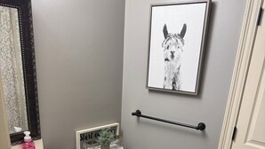 A bathroom with a toilet, sink, and mirror. There is a framed picture on the wall and a towel rack.