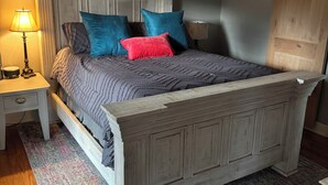 A bedroom with a wooden bed, a nightstand with a lamp, a ceiling fan, and a wooden wardrobe.