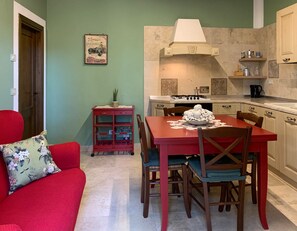Un espace de vie compact comprenant une table à manger, des chaises, un canapé, un coin cuisine et un petit meuble de rangement.