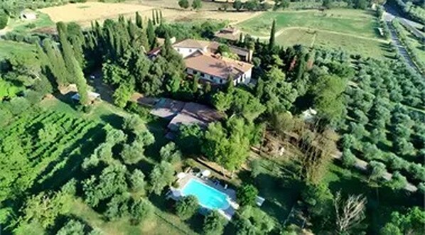 Vista aérea de uma propriedade residencial com piscina, cercada por vegetação densa e uma casa grande com telhado inclinado.