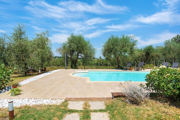 A swimming pool with a curved edge, surrounded by a paved deck and a stone border. - Agriturismo Santa Luce – 'Lavanda' Apartment with Shared Pool, Private Garden and Wi-Fi (Foiano della Chiana)
