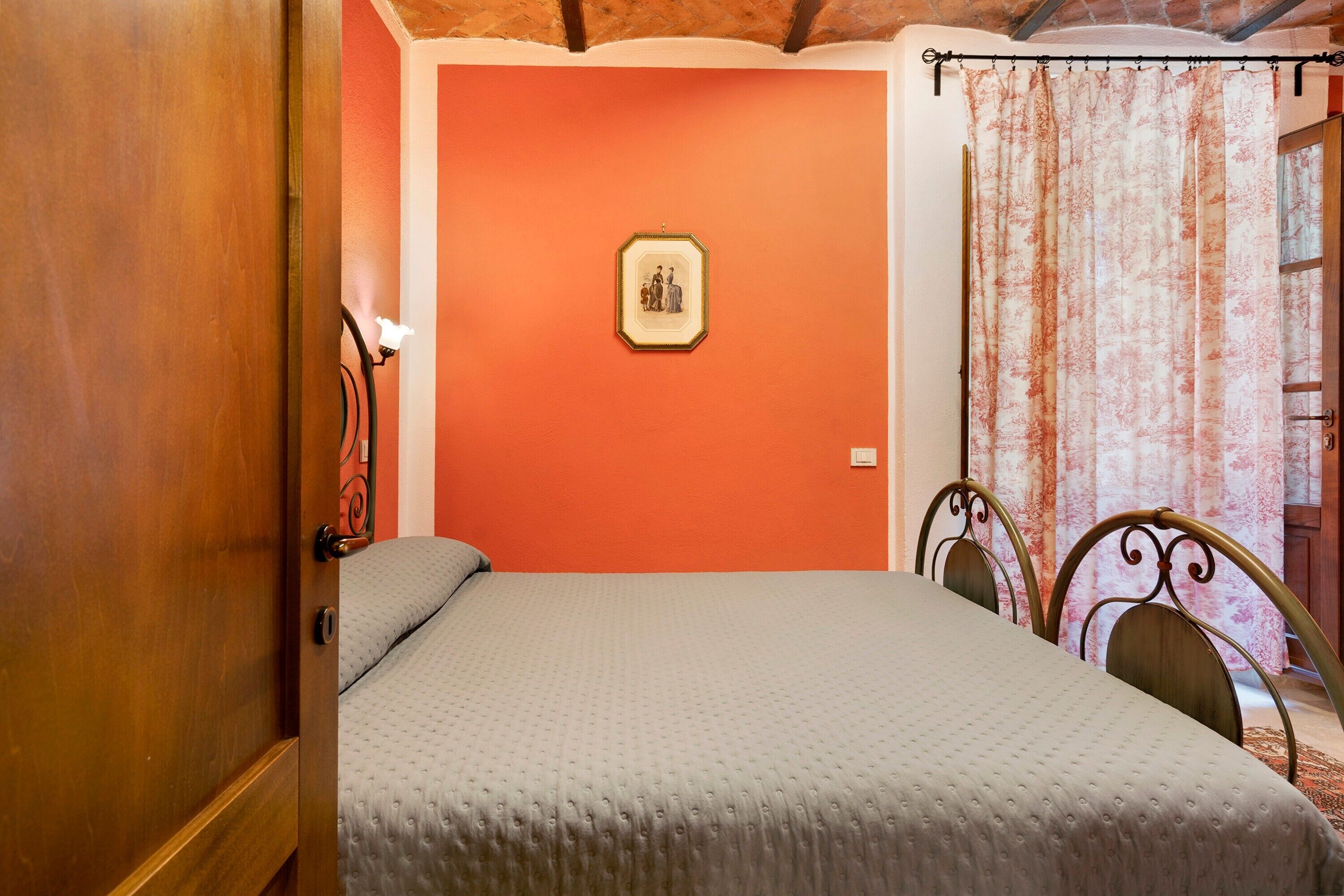 Ein Schlafzimmer mit einem Bett, einer Tür, einem gerahmten Bild an der Wand und einem Vorhang.