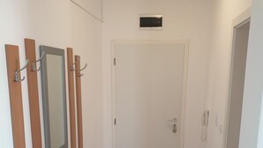 A hallway with a white door, a coat rack with several coats, a small mirror, and a telephone.