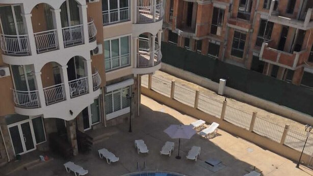 A swimming pool with sun loungers and umbrellas, surrounded by a building with balconies.