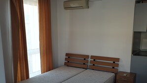 A bedroom with a bed, a nightstand, a wall-mounted air conditioner, and a window with curtains.