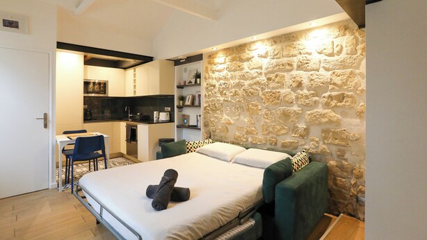 A compact room with a bed, a small kitchenette, and a stone wall. - Charming  studio in the 17th, ideal for 2 (Paris)