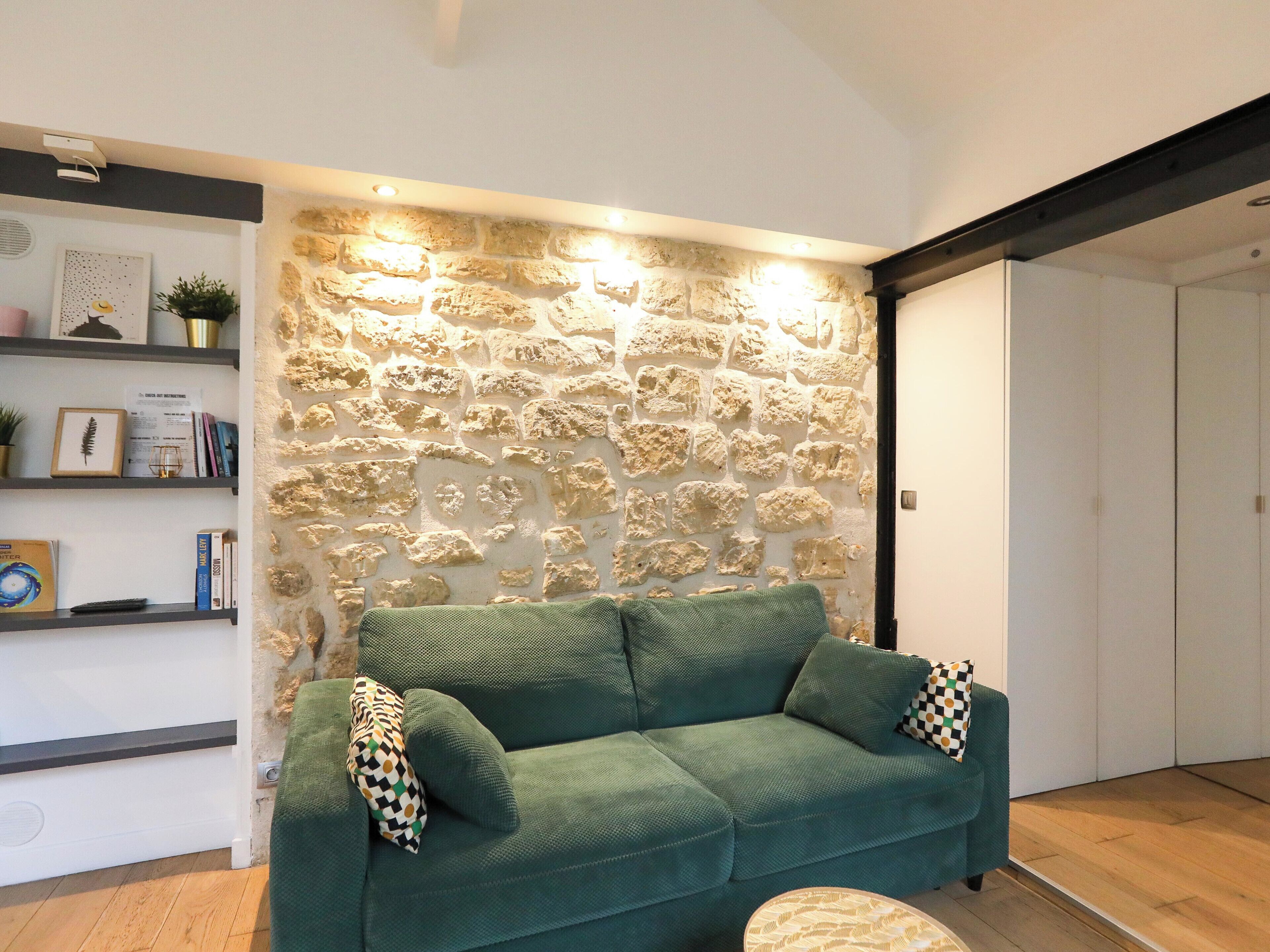 A living room with a stone wall, a green sofa, and a bookshelf.