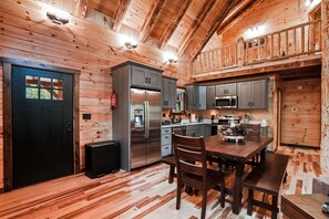 Interior de una cabaña de madera con cocina, comedor y una puerta negra.