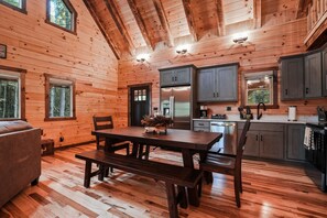 Interior de una cabaña de madera con una mesa de comedor, bancos, un refrigerador y armarios.