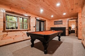 Un intérieur en bois avec une table de billard, une cheminée et une enseigne indiquant « Billard ».