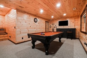 A pool table in a room with wooden walls and a television mounted on the wall.