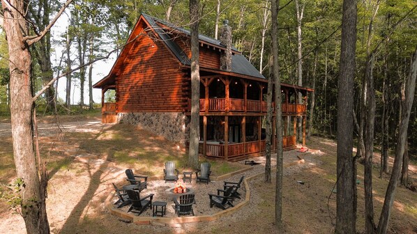 A log cabin with a stone foundation, a balcony, and a fire pit with chairs.