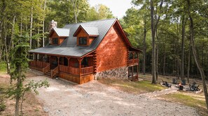 A log cabin with a porch, a stone foundation, and a fire pit area.