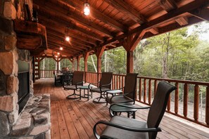 A covered deck with stone walls, wooden flooring, and outdoor seating.