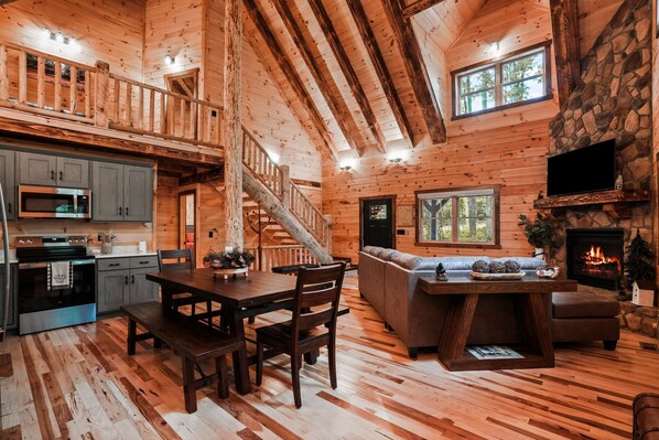 A wooden cabin interior with a dining area, kitchen, living room, and fireplace. - Timberland Ridge | Hocking Hills, New, Hot Tub (Logan)