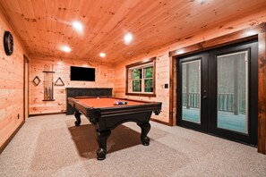 A wooden-paneled room with a pool table, a television, and a door leading to an outdoor area.