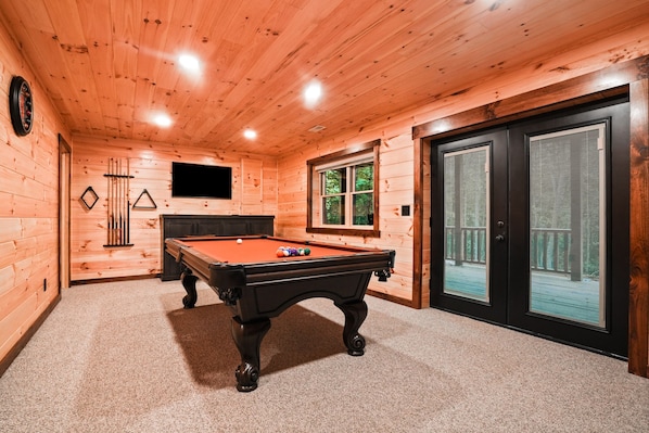 A wooden-paneled room with a pool table, a television, and a door leading to an outdoor area. - Timberland Ridge | Hocking Hills, New, Hot Tub (Logan)