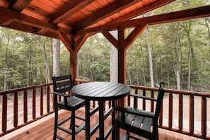 A wooden deck with a table and chairs, surrounded by a forest. - Timberland Ridge | Hocking Hills, New, Hot Tub (Logan)