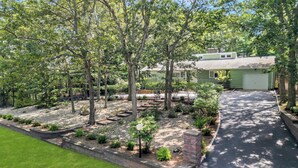 Una propietat residencial amb una casa verda, una entrada de cotxes i un jardí ben cuidat amb plantes i arbres diversos.